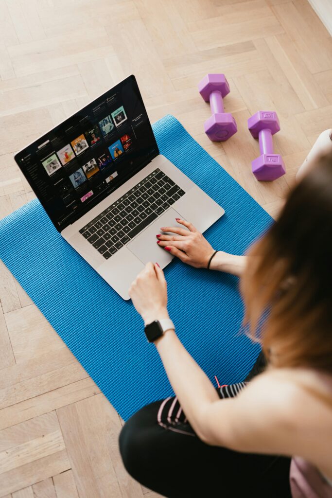 From above of anonymous female surfing laptop while during exercising on blue yoga mat